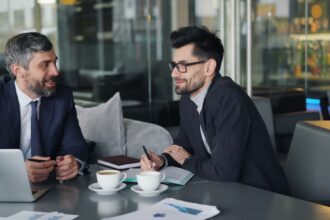 a couple of men sitting at a table in front of a laptop