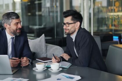 a couple of men sitting at a table in front of a laptop