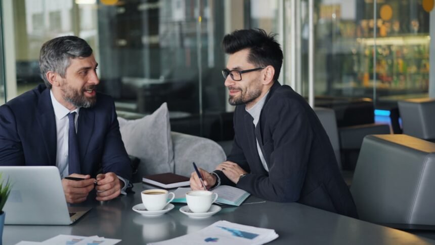 a couple of men sitting at a table in front of a laptop