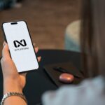 Person holding a smartphone with a logo on screen.