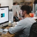 man in gray sweatshirt sitting on chair in front of iMac