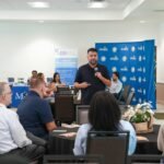 A man speaking into a microphone at a business conference with seated attendees