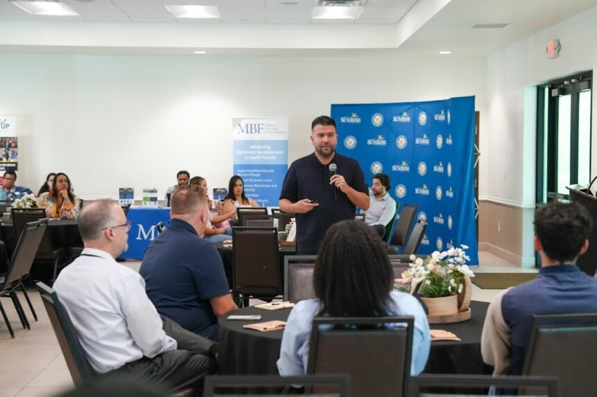 A man speaking into a microphone at a business conference with seated attendees